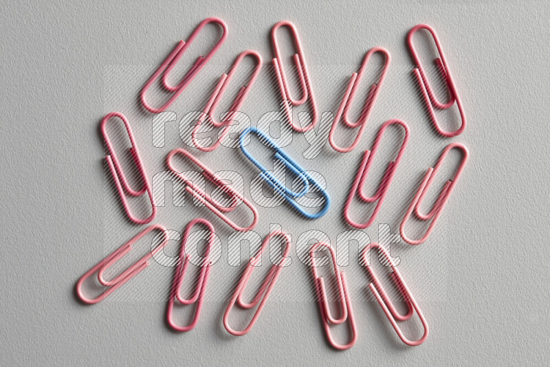 A blue paperclip surrounded by bunch of pink paperclips on grey background