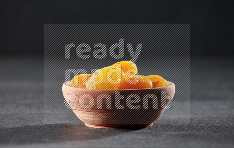 A wooden bowl full of dried apricots on a black background in different angles