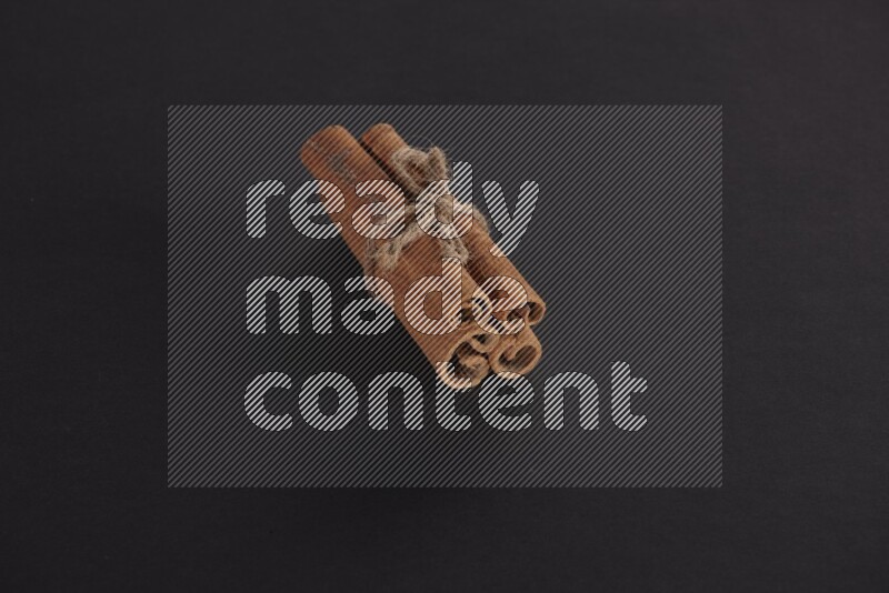 4 Cinnamon sticks stacked and bounded on black flooring
