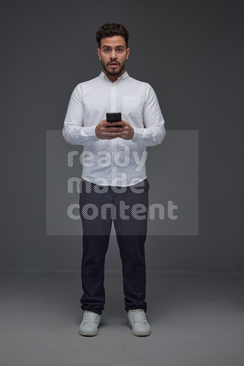 A man wearing smart casual standing and using his phone eye level on a gray background