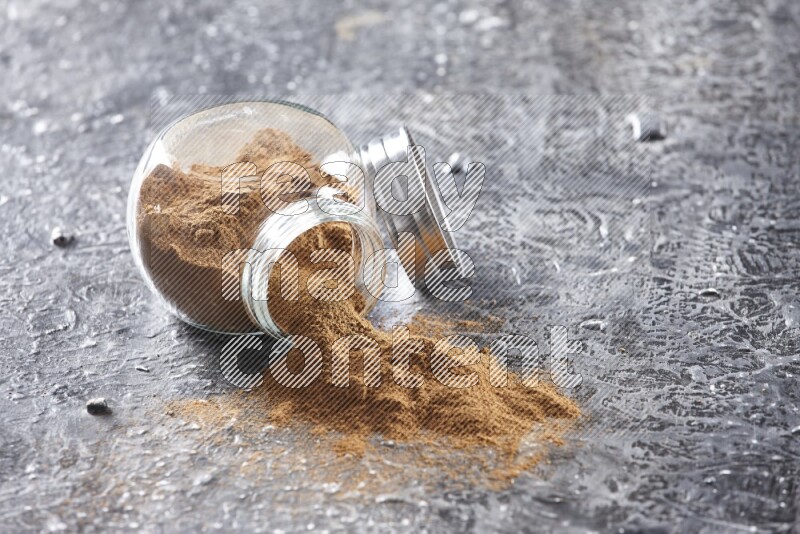 Flipped herbal glass jar full of cinnamon powder on textured black background