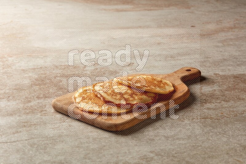 Three stacked plain pancakes on a wooden board on beige background