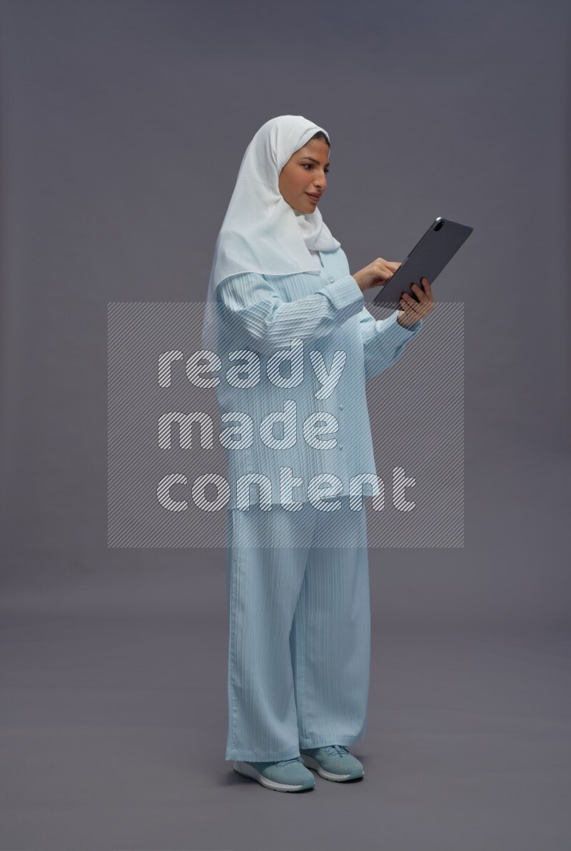 Saudi woman wearing hijab clothes standing working on tablet on gray background