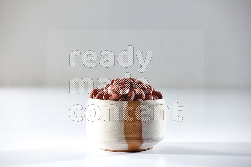 A beige ceramic bowl full of red skin peanuts on a white background in different angles