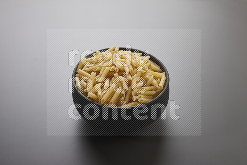 Mini penne pasta in a pottery bowl on grey background