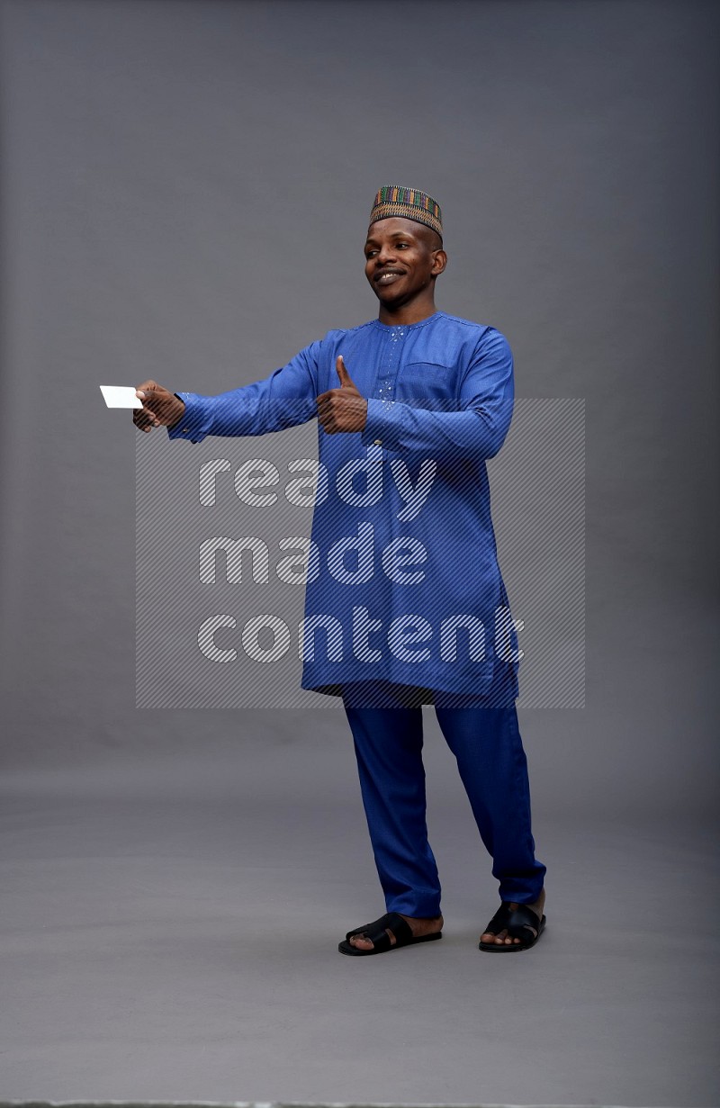 Man wearing Nigerian outfit standing holding ATM card on gray background