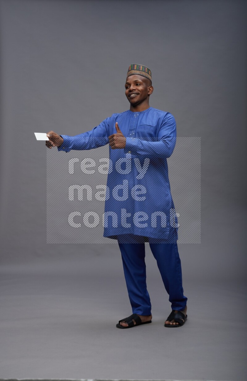 Man wearing Nigerian outfit standing holding ATM card on gray background