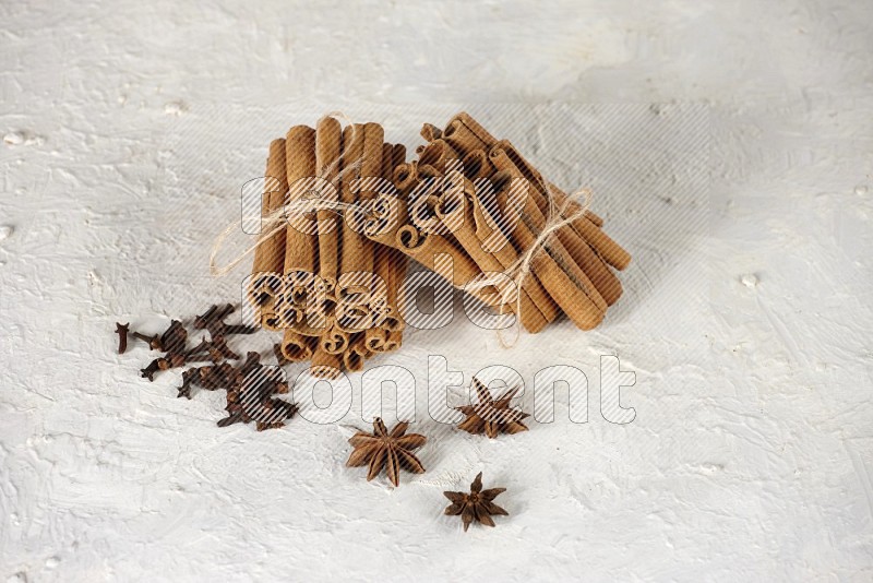 Two bounded stacks of cinnamon sticks with cloves and star anise on white background