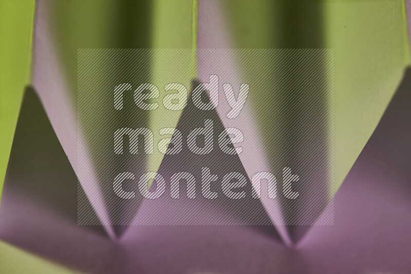 A close-up abstract image showing sharp geometric paper folds in green and pink gradients