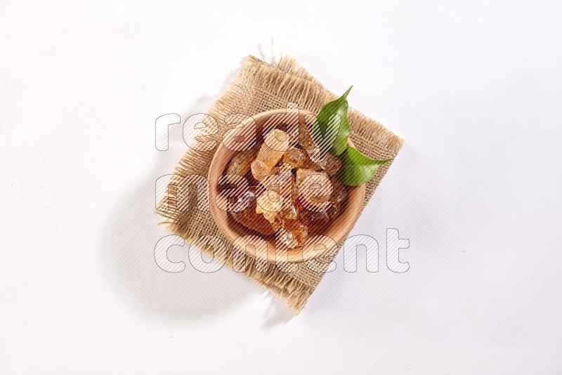 A wooden bowl full of gum arabic on a piece of burlap on white flooring in different angles