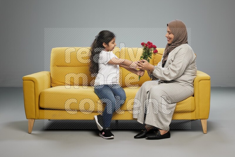 A girl sitting giving flowers to her mother on gray background