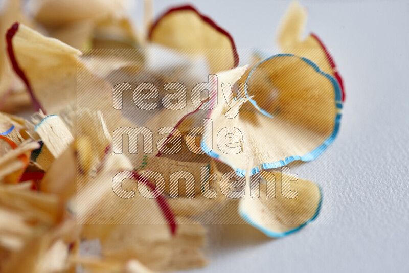 A close-up showing a small pile of pencil shavings with varied color edges on grey background