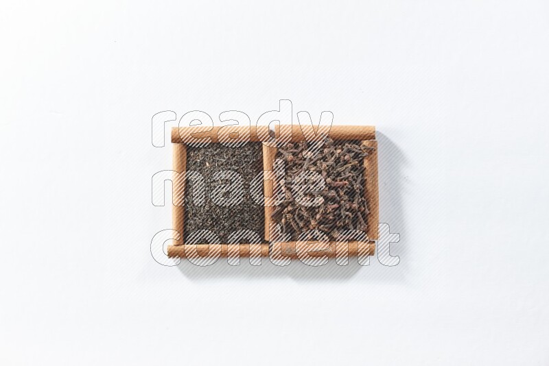 مربعان من أعواد القرفة ممتلئان بالشاي الأسود وحبوب القرنفل علي خلفية بيضاء