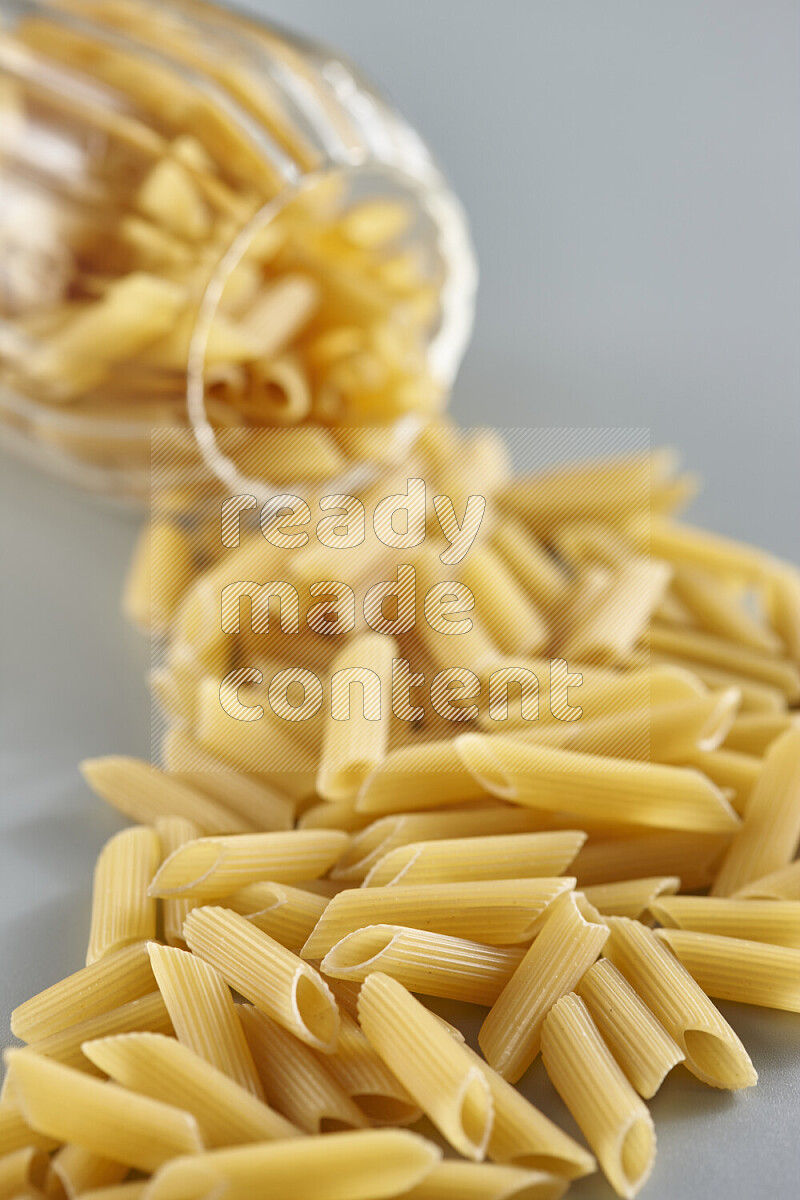 Flipped jar full of raw pasta on light blue background
