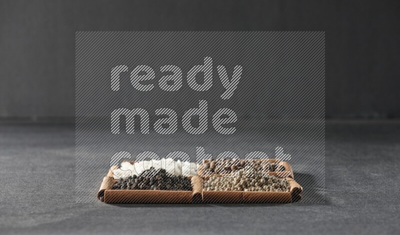 4 مربعات من عيدان القرفة ممتلئة بحبوب الفلفل الأسود والفلفل الأبيض وبهار الفلفل الحلو والملح الأبيض على أرضية سوداء