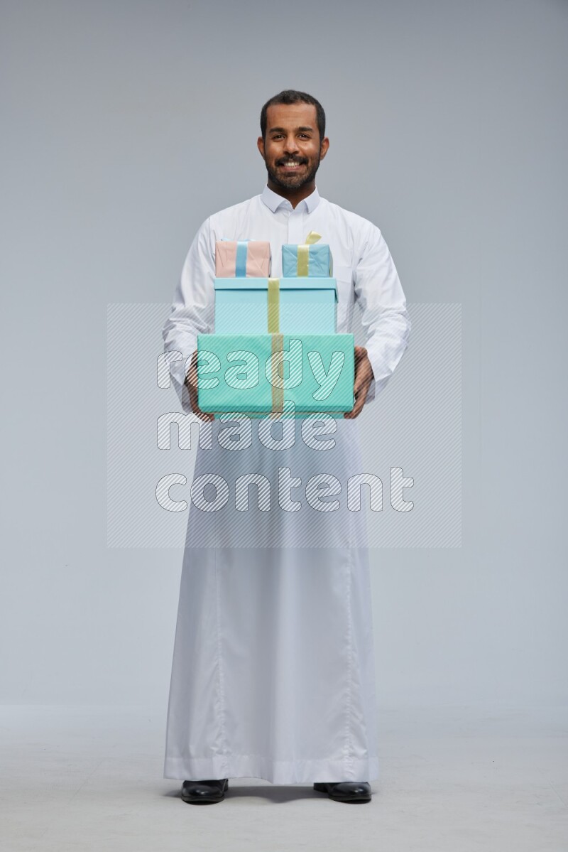 Saudi man Wearing thob standing holding gift box on Gray background