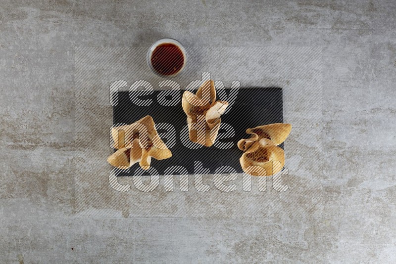 wonton cups with soy sauce ramkin on rectangle slate on grey textured counter top