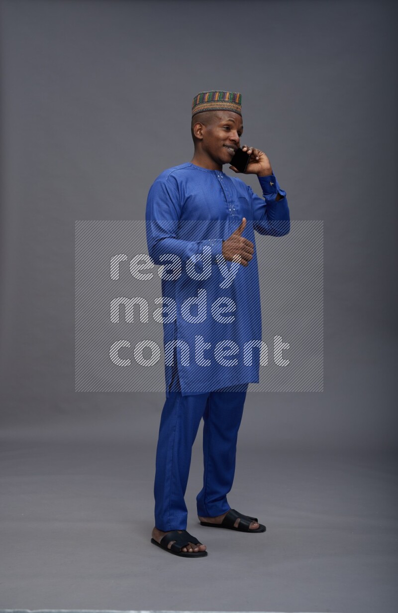 Man wearing Nigerian outfit standing talking on phone on gray background