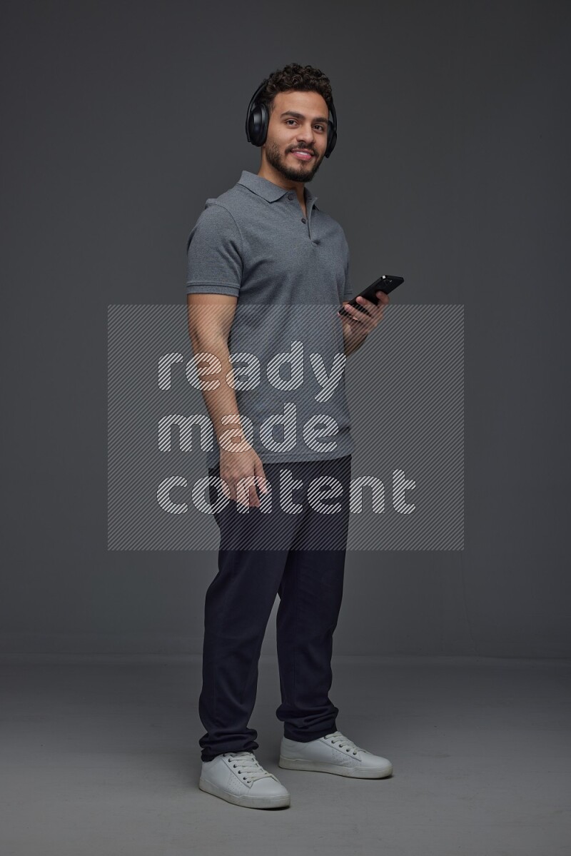 A man wearing casual and using his phone and headphone eye level on a gray background