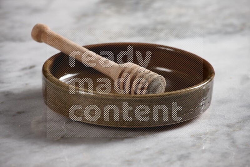 Multicolored pottery oven plate with wooden honey handle in it on grey marble background