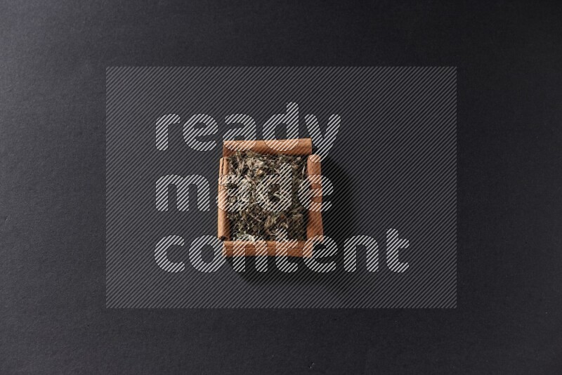 أربعة من أعواد القرفة مكونة شكل مربع بداخلها ريحان مجفف علي خلفية سوداء