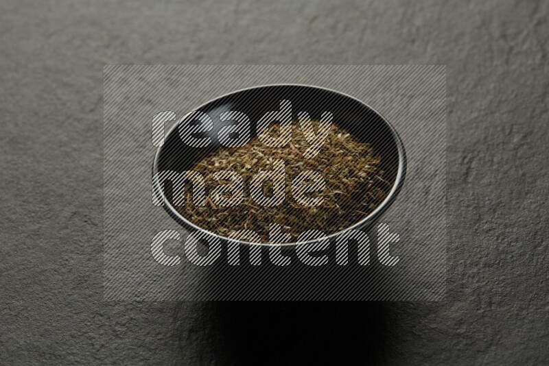 black pottery round sauce bowl filled with herbs on grey textured countertop