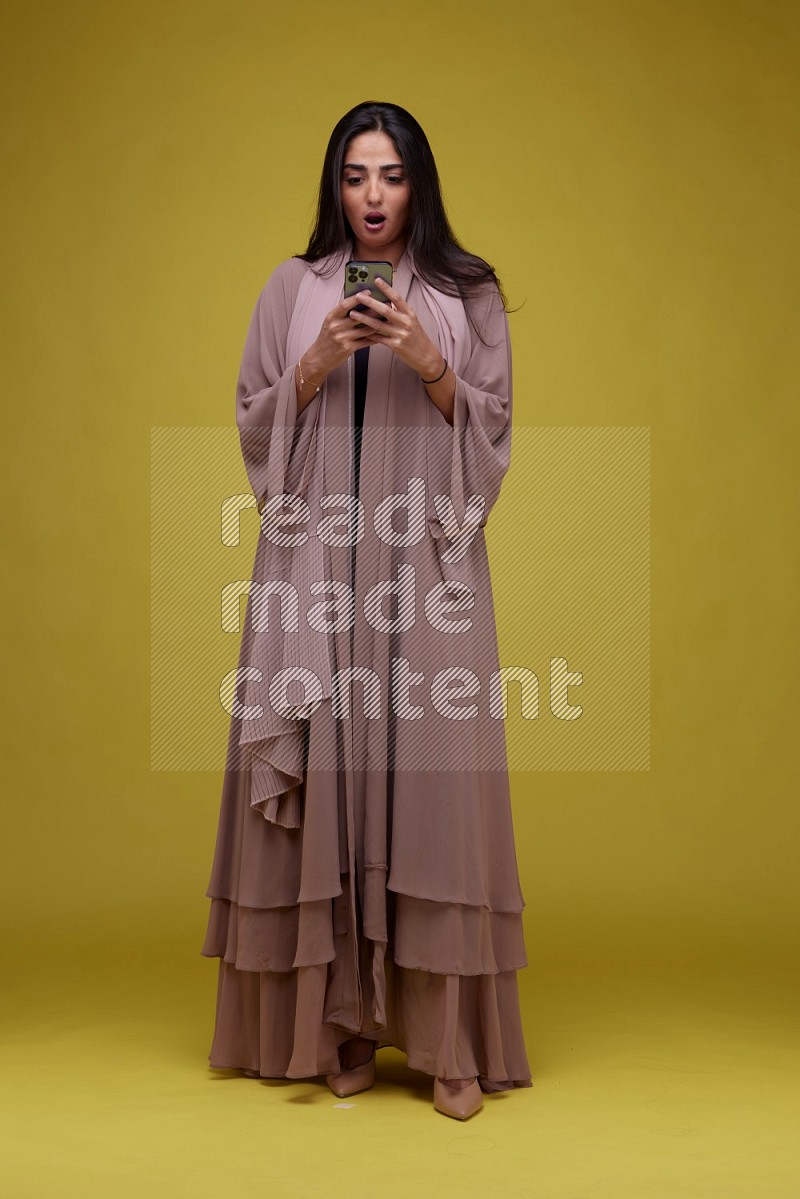 A woman Texting on a Yellow Background wearing Brown Abaya