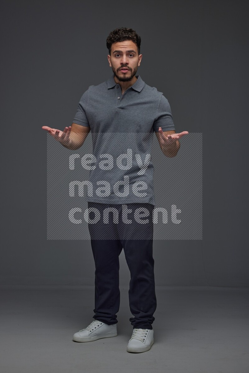 A man wearing casual standing and making multi hand gestures eye level on a gray background
