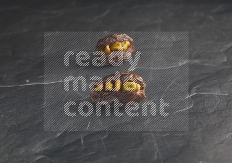 two pistachios stuffed madjoul dates on a black textured background