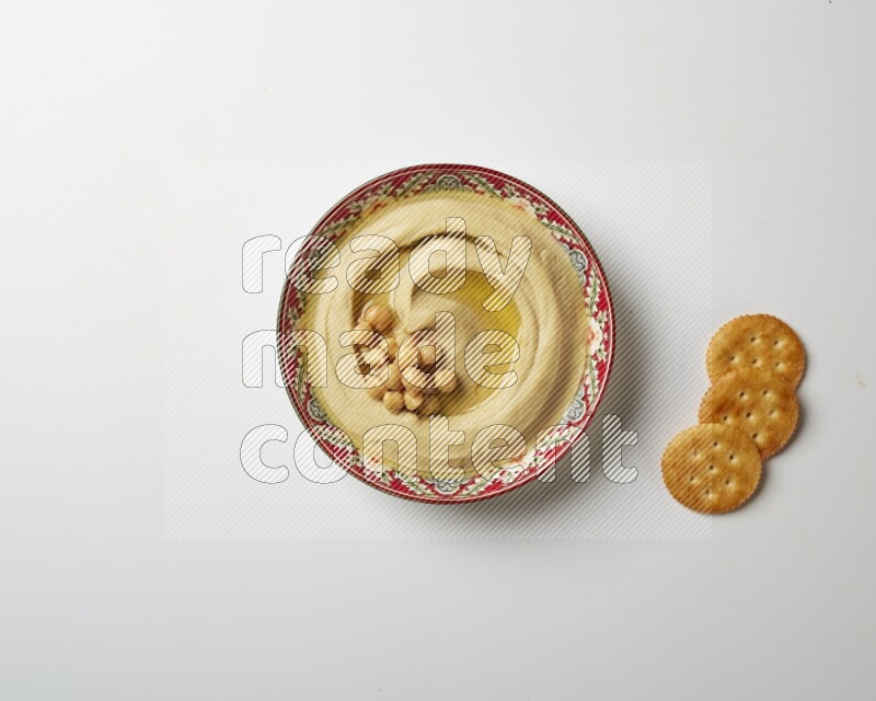 Hummus in a red plate with patterns garnished with roasted chickpeas  on a white background