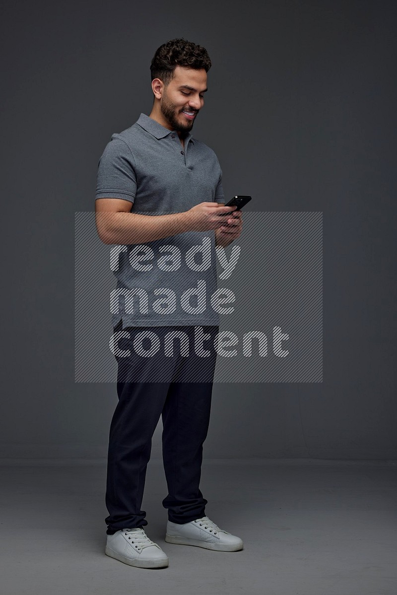 A man wearing casual standing and using his phone eye level on a gray background