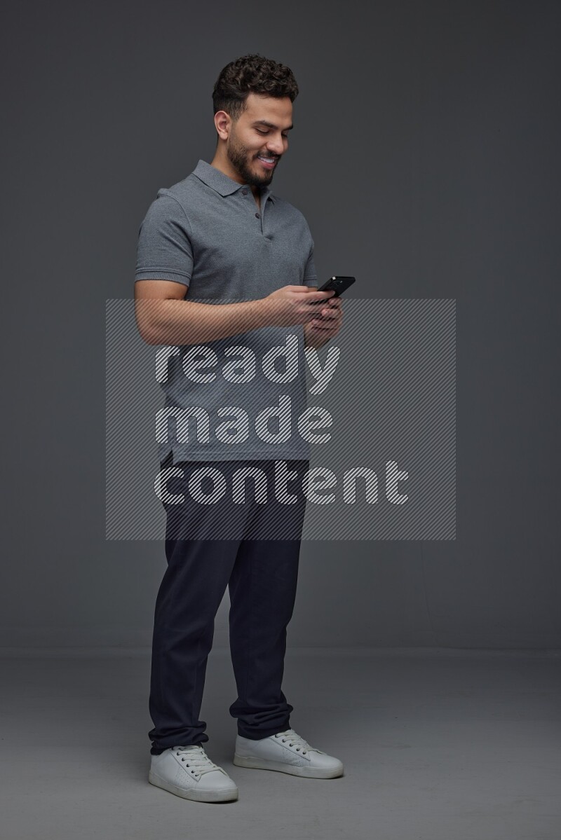 A man wearing casual standing and using his phone eye level on a gray background