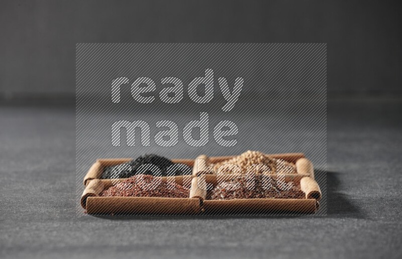 4 squares of cinnamon sticks full of flaxseeds, garden cress, black seeds and mustard seeds on black flooring