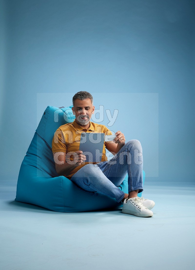 A man sitting on a blue beanbag and holding ATM card with tablet