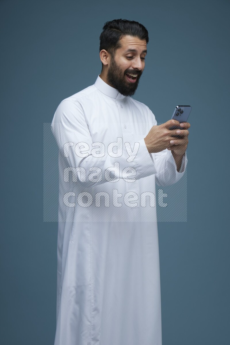 A man Texting in a blue background wearing Saudi Thob