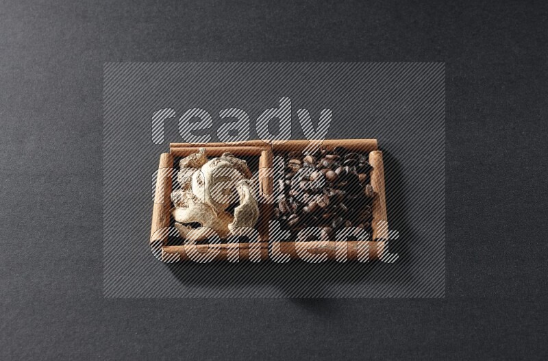 مربعان من أعواد القرفة ممتلئان بحبوب القهوة والزنجبيل المجفف علي خلفية سوداء