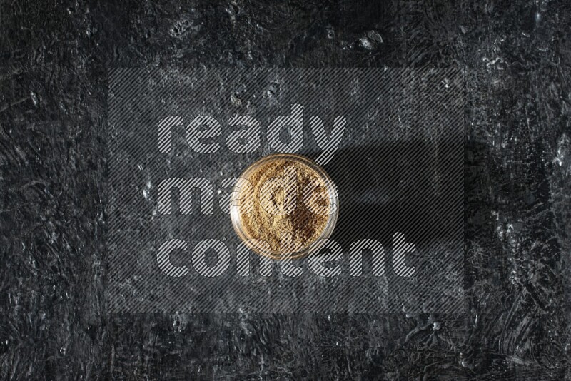 A glass jar full of allspice powder on a textured black flooring
