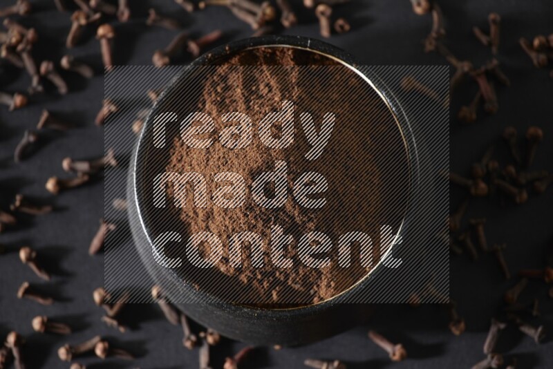 وعاء فخاري أسود ممتلئ ببودرة القرنفل وحبوب القرنفل على خلفية سوداء