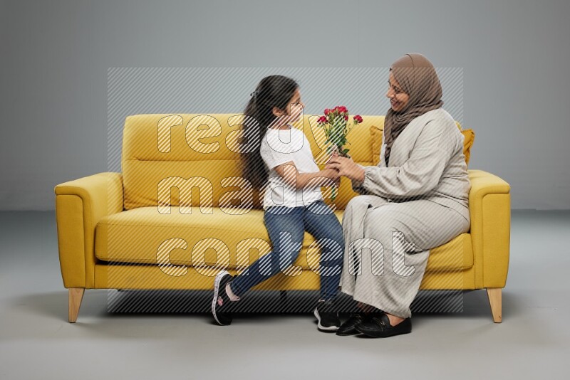A girl sitting giving flowers to her mother on gray background