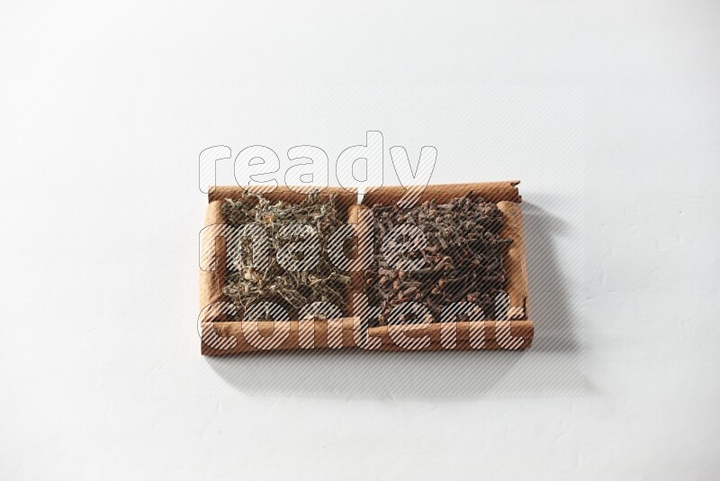 2 squares of cinnamon sticks full of cloves and dried basil on white flooring