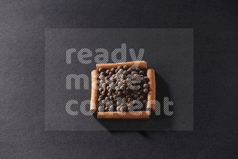 A single square of cinnamon sticks full of allspice on black flooring