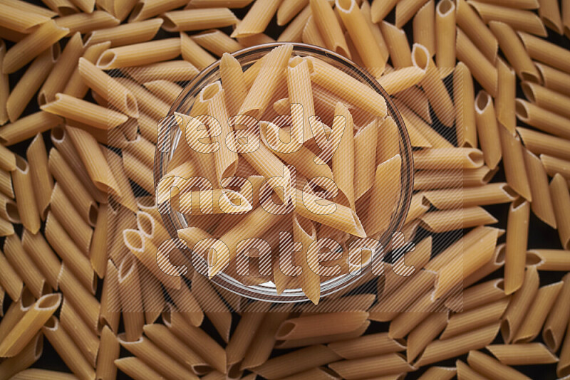 Penne pasta in a glass bowl on black background