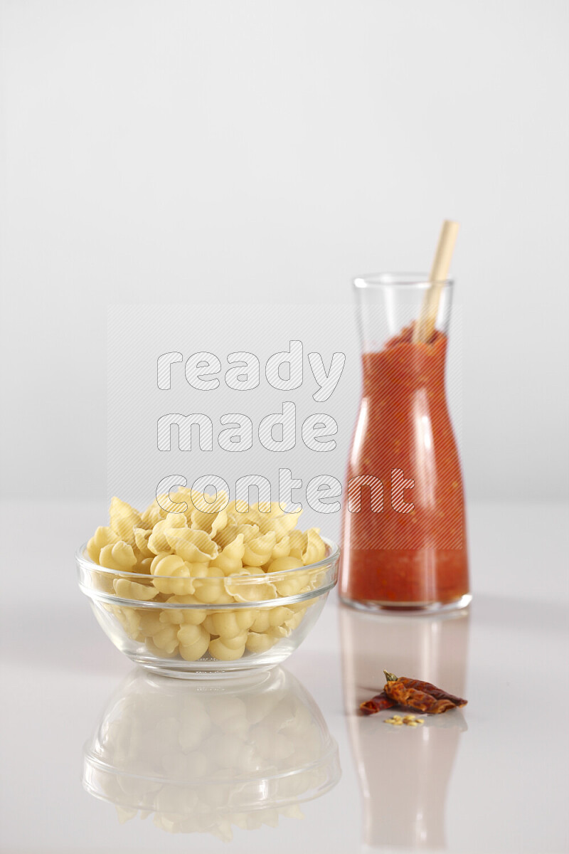 Raw pasta with tomatoe pasta with different ingredients such as cherry tomatoes, basil, garlic, bay laurel, cardamom, white pepper, black pepper, red chilis and wheat stalks on light grey background