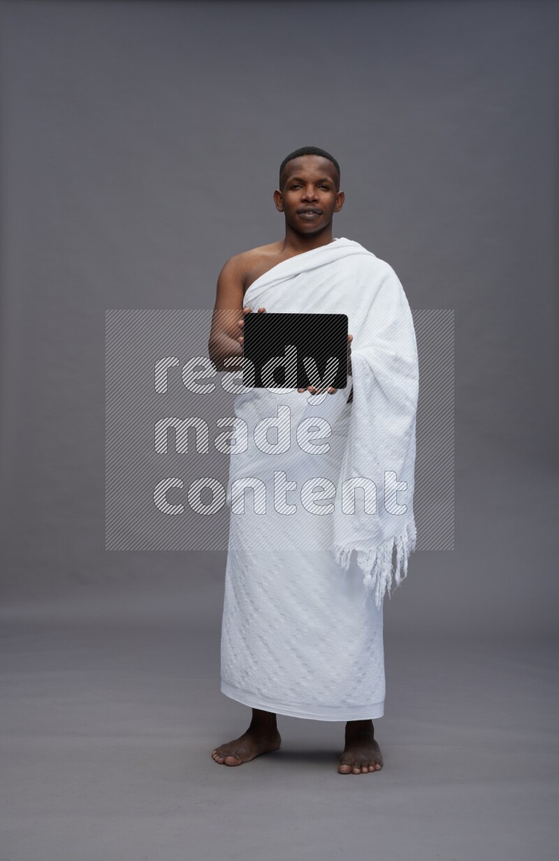 A man wearing Ehram Standing showing tablet to camera on gray background