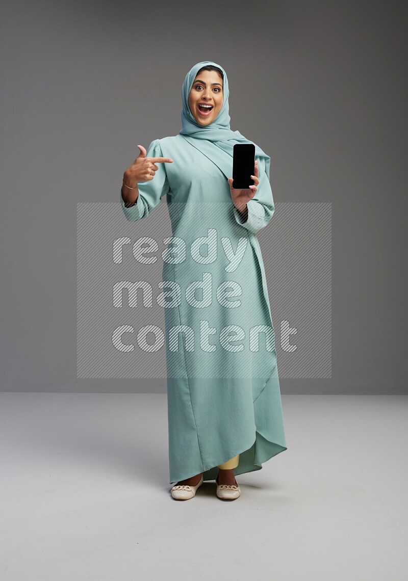 Saudi Woman wearing Abaya standing showing phone to camera on Gray background