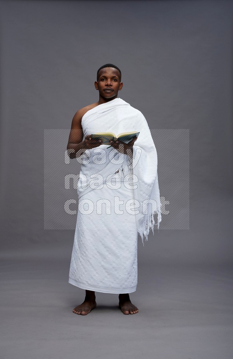 A man wearing Ehram Standing reading quran on gray background