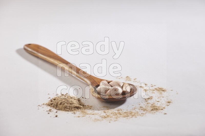 A wooden ladle full of garlic cloves with sprinkled powder on a white flooring