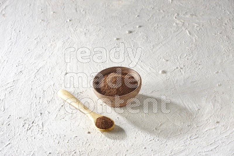 A wooden bowl and a wooden spoon full of cloves powder on a textured white flooring