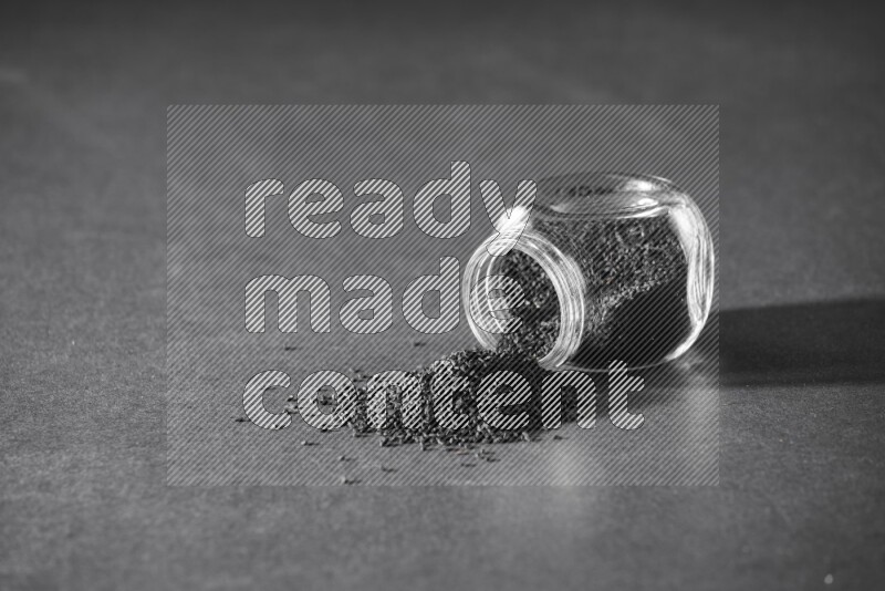 A flipped glass spice jar full of black seeds and the seeds spread out on a black flooring