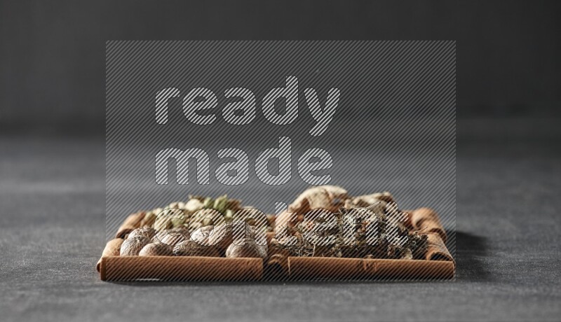 4 مربعات من عيدان القرفة ممتلئة بالريحان المجفف والهيل والزنجبيل المجفف وجوزة الطيب على أرضية سوداء